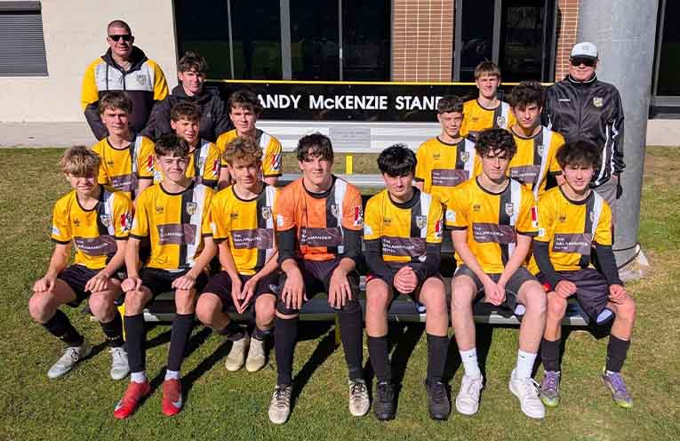 Nelson Bay’s championship-winning under-16 players in front of the new Andy McKenzie Stand that perpetuates the memory of club legend Andy McKenzie. Photo: Nelson Bay FC.